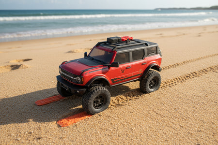 Red toy truck on a sandy beach with ocean waves in the background